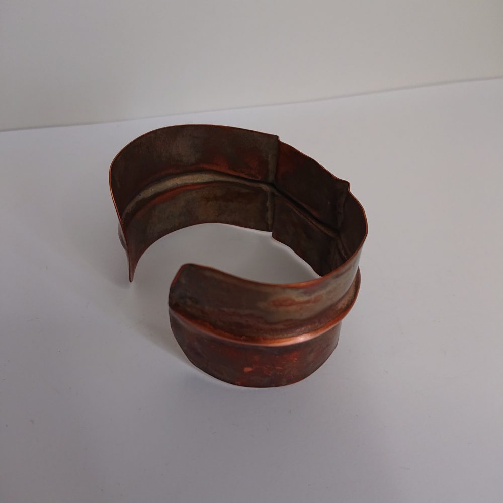Chunky copper cuff bracelet or bangle with aged copper colour patina and fold formed design, showing the back of the design