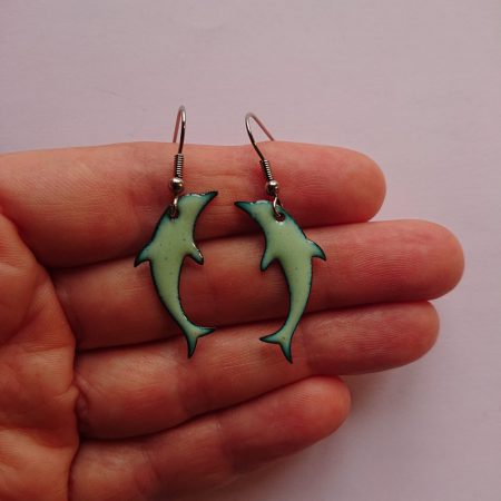 Pale green overfired enamelled copper dolphin shaped earrings with allergy safe surgical steel hooks being held
