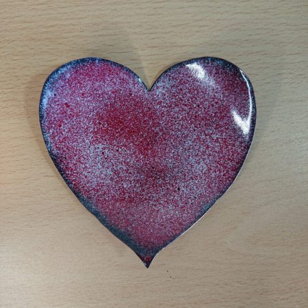 Handmade heart shaped enamelled copper decorative bowl or dish. The bowl or dish is quite shallow. It is red with lots of tiny white dots. It has been given longer in the kiln to give a dark edge and dark dots. The rim edge is bright shiny copper.