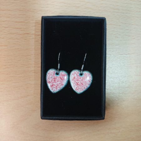 White, heart shaped enamelled copper earrings with red dots. Handmade. The white is a tiny bit creamy or ivory. The red dots are tiny. The earhooks are allergy safe surgical steel and they're in a black presentation box.