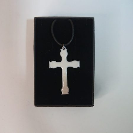 White enamelled copper necklace in a cross or crucifix shape. The white is a little creamy or ivory, rather than a sharp white. It's in its black presentation box.