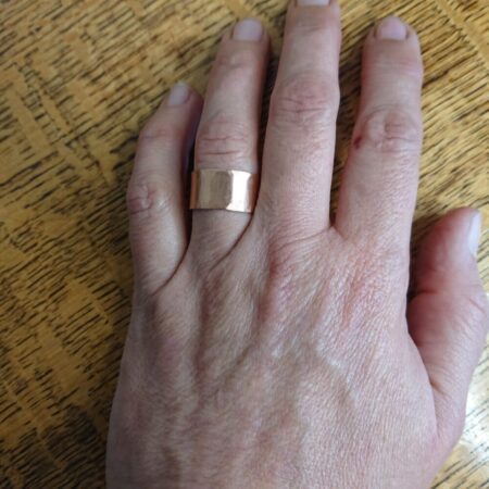 Bright shiny copper cuff ring made from flat sheet copper. The ring is a chunky, plain band with light hammer marks. This photo shows it being worn.