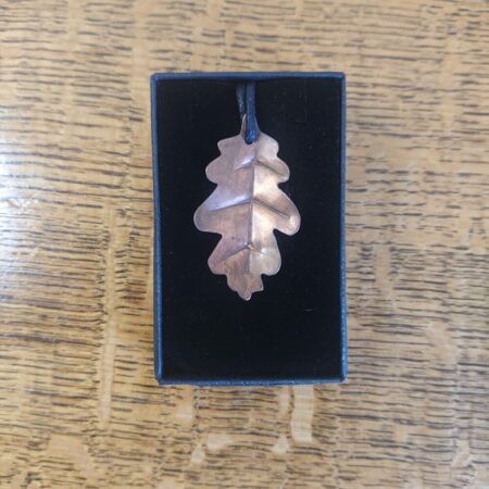 Copper oak leaf shaped necklace pendant, handmade, on a black waxed cotton cord. The leaf has veins stamped into it, which also means it isn't flat. The copper has an aged copper colour patina - a mid brown shade. This photo shows the necklace in its black presentation box