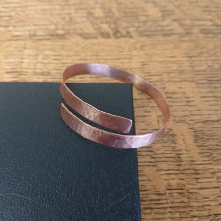 Copper bracelet or bangle with hammer marks and small overlap. The copper strip of the bracelet is about 0.7cm wide. The bracelet is shiny, bright copper (finished with lacquer). This picture shows it resting on the lid of its presentation box