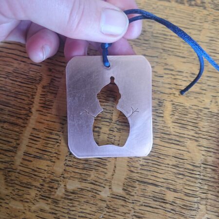 Copper Christmas decoration of a snowman cut out of a rectangle of flat shiny copper. It has a dark blue coloured cord for hanging.