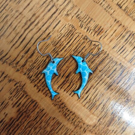 Dolphin shaped enamel copper earrings with blue bit dots on a creamy white background. Surgical steel ear hooks