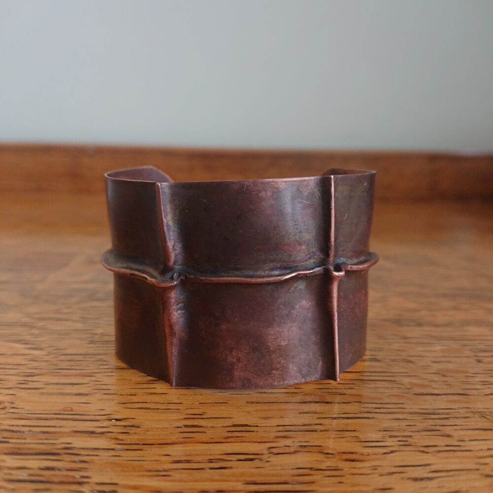 Copper bracelet with fold-formed ridges in a chunky cuff style. There is a centre ridge line, plus two vertical ridge or fold lines. It has an aged copper colour patina, so a mid to darker brown