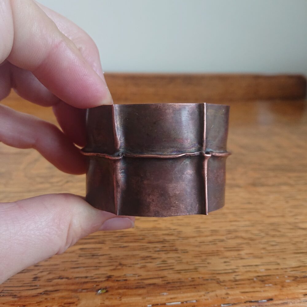 Copper bracelet with fold-formed ridges in a chunky cuff style. There is a centre ridge line, plus two vertical ridge or fold lines. It has an aged copper colour patina, so a mid to darker brown