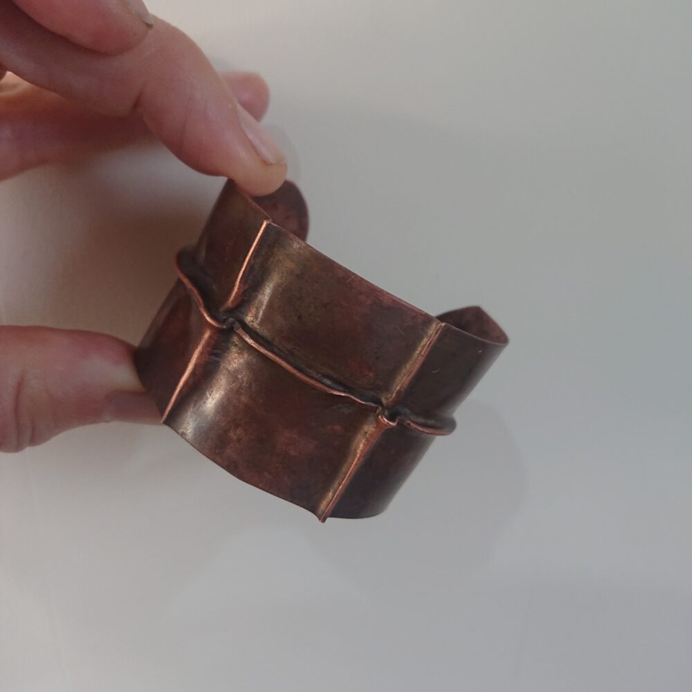 Copper bracelet with fold-formed ridges in a chunky cuff style - perhaps industrial, perhaps bohemian. It has an aged copper colour patina, so a mid to darker brown