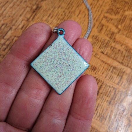 Enamelled copper necklace that's square, but hung by a corner so more of a diamond orientation. The pendant is pale green with other colours mixed in and a darker outer edge.