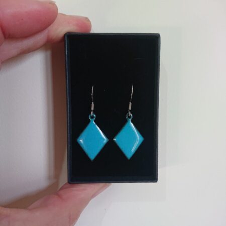 Teal diamond or trapezoid shaped earrings with ear hooks and in a black presentation box. The teal colour is turquoise blue to my eyes. I fired them for longer to give tiny darker dots to make them more interesting.