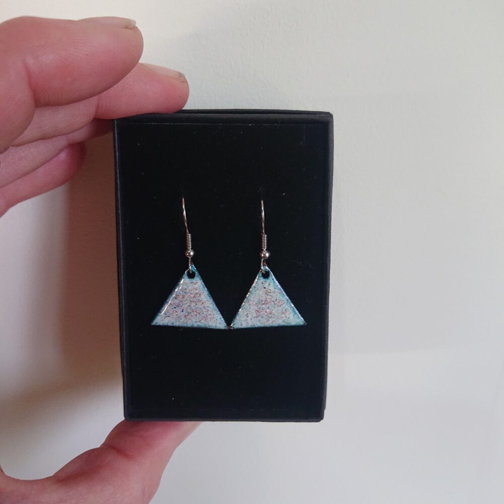 Triangle or triangular shaped earrings with ear hooks. The earrings have pale backgrounds with lots of tiny coloured dots or spots. They are shown in their black presentation box.