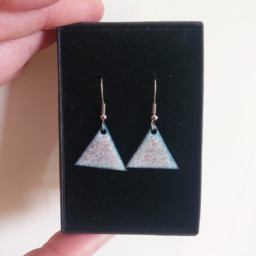 Triangle or triangular shaped earrings with ear hooks. The earrings have pale backgrounds with lots of tiny coloured dots or spots. They are shown in their black presentation box.