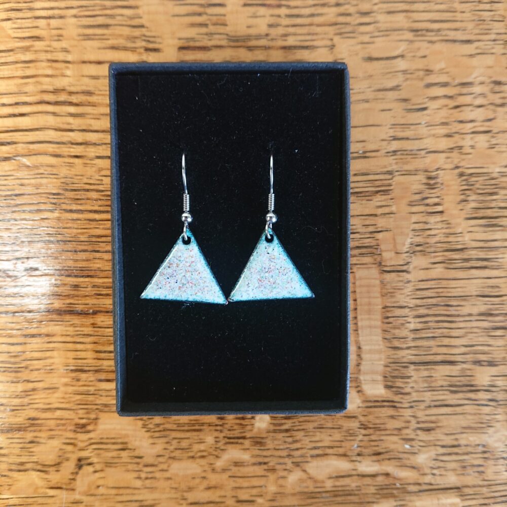 Triangle or triangular shaped earrings with ear hooks. The earrings have pale backgrounds with lots of tiny coloured dots or spots. They are shown in their black presentation box.