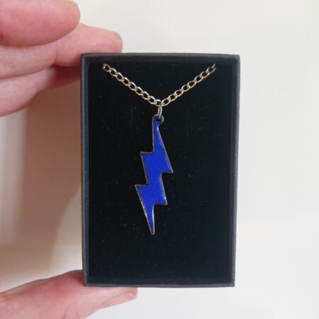 Royal blue lightning shaped necklace pendant made from enamel on copper. The pendant has a silver coloured chain and is in its presentation box. The blue has a slightly darker outer edge.