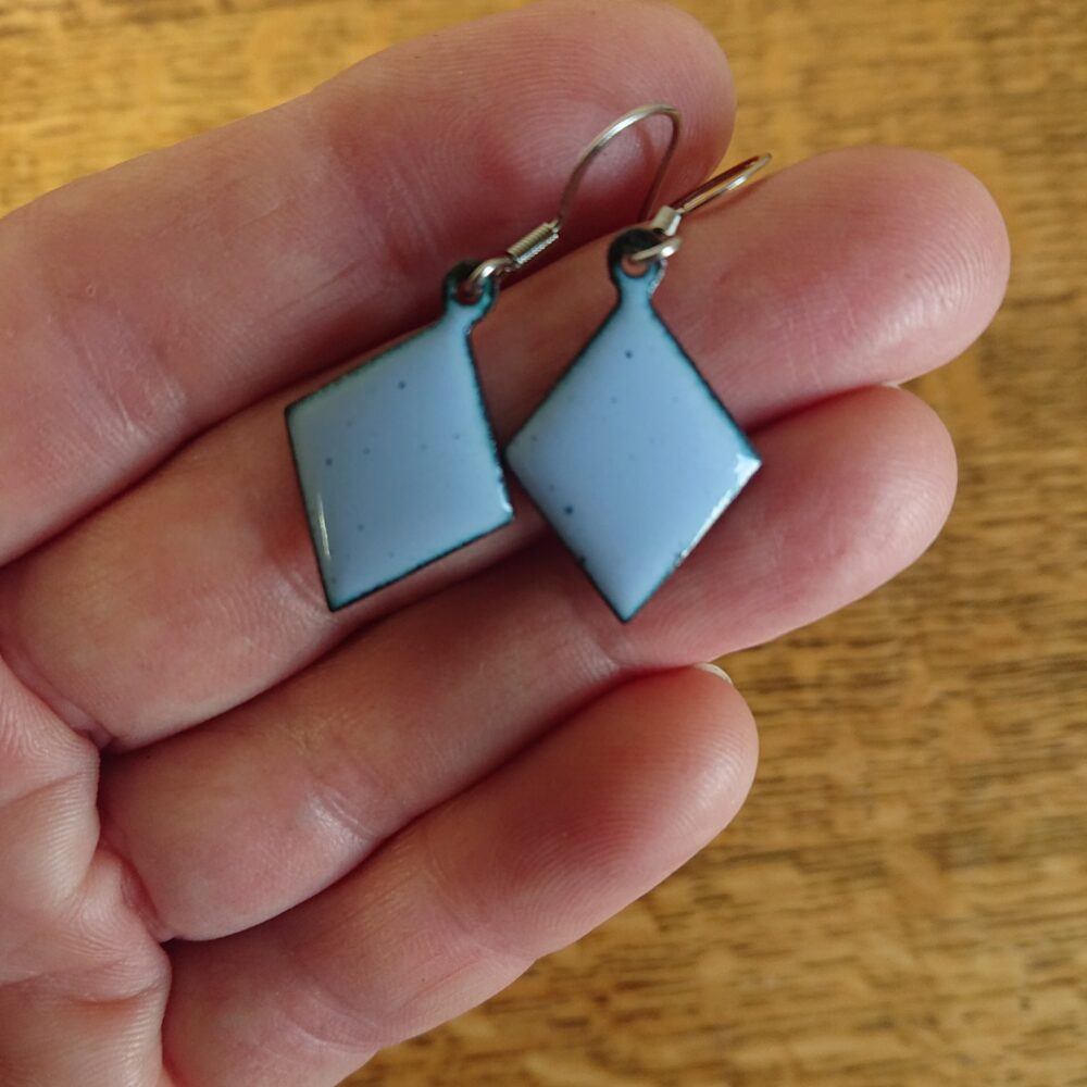 Light grey with a lilac tint enamelled copper earrings. The earrings have been fired for longer so have dark dots. They're on ear hooks. The shape is diamond or trapezoid.