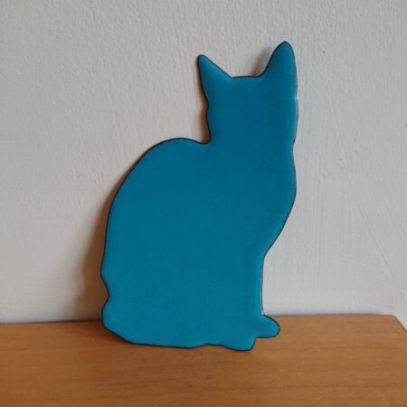 Sitting cat wall hanging or wall art. The cat is enamelled in teal, so a turquoise shade around blue and green. It has tiny darker dots in the enamel and a thin darker outer edge. The cat has no features, like a silhouette. It has no frame.